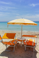 Beach equipment, chairs and sun umbrella on white sandy beach with light blue sea water, beach vacation concept