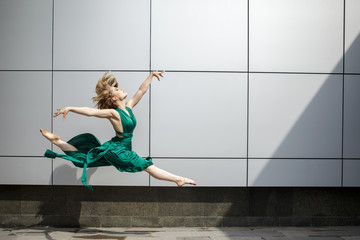 Beautiful girl dancing in the city and jumping against the wall background.