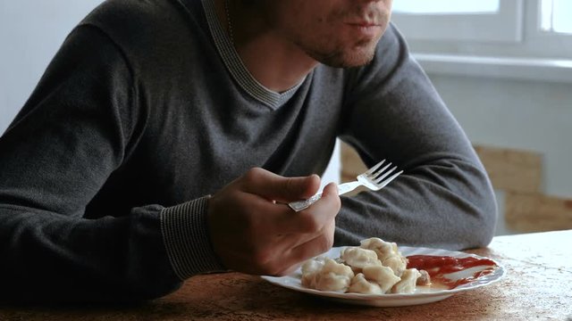 Man eats dumplings with a fork, putting them into tomato sauce in the kitchen