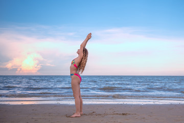 Fototapeta na wymiar Young healthy woman with blonde curly hair doing yoga on the beach, heathy and relaxing concept.