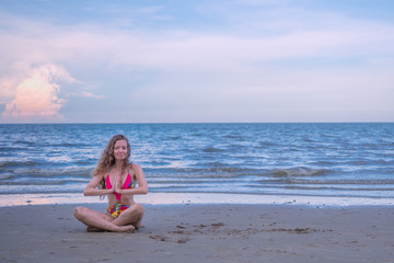 Young healthy woman with blonde curly hair doing yoga on the beach, heathy and relaxing concept.