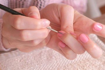 Woman puts first coat of pink shellac on her nails with small tassel. Close-up hands.