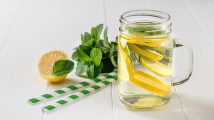 A refreshing drink of lemon, mint and ginger root slices on a white table.
