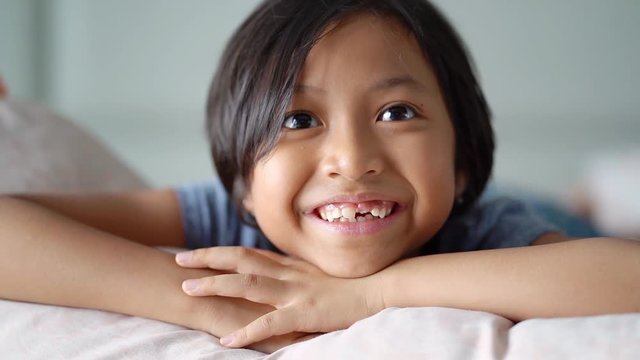 Cute little girl smiling at the camera with her first lost milk tooth, lying on the bedroom while watching TV at home