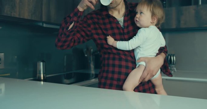 Father with toddler in kitchen drinking coffee