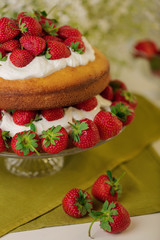 Homemade strawberry cake with cream on a glass stand.