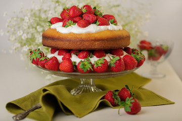 Homemade strawberry cake with cream on a glass stand.