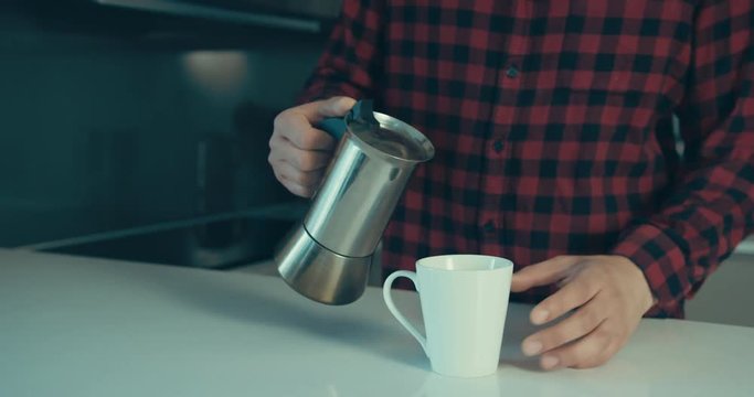 Young man in hipster shirt pouring coffe in his kitchen