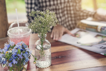 Young woman reading magazine at restaurant with juice and bouquet