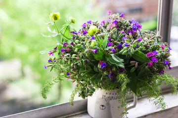 Wild forest meadow bouquet of cherry, lungwort, wild herbs in ceramic cup on window sill