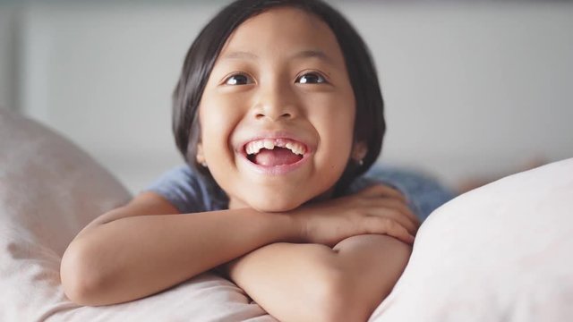 Cheerful toothless little girl watching TV while laughing and lying in the bedroom at home. Shot in 4k resolution
