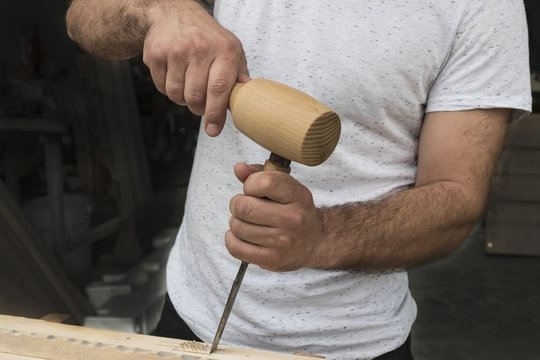 The carpenter in a white T-shirt works as a chisel and a mallet