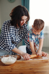 Mother and son dressed in plaid shirts are cooked in the kitchen of flour and dough