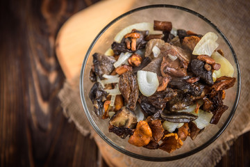 Golden fried forest mushrooms with onion in a bowl on wooden background with copy space.
