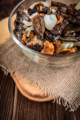 Golden fried forest mushrooms with onion in a bowl on wooden background with copy space.