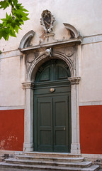 Fototapeta na wymiar Old Church door in Venice. Italy. The door is decorated with bas-reliefs and decorative elements. Above the door is a skull sculpture