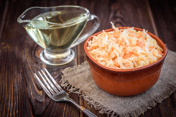 Fresh vegan salad with carrots and cabbage with vegetable oil in a bowl on a dark wood background.