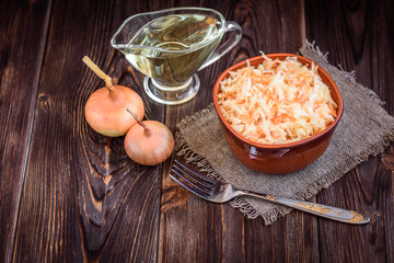 Fresh vegan salad with carrots and cabbage with vegetable oil in a bowl on a dark wood background.