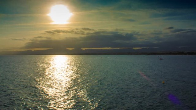 Sunset in the clouds and mountains on the sea in the tourist season with boats and parachute