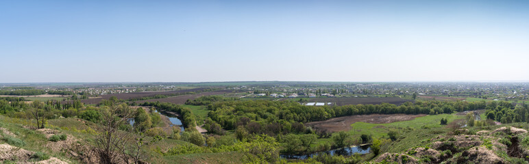 Fototapeta na wymiar Panorama. View from the hill to the lake, fields and a small town