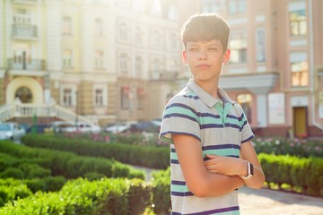 Outdoor portrait of teenager 13, 14 years old, boy with crossed arms, urban background