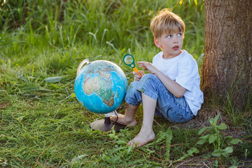 Side view of cute preschooler boy researcher with earth globe and the magnifying glass in the park. Adventure, dreaming about traveling life concept.