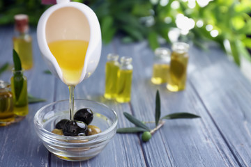 Pouring oil into bowl with olives on wooden table