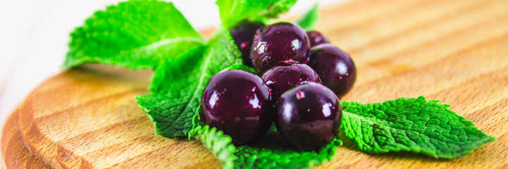 Black currant on a blackboard with a straw and smoothies on a white wooden table.