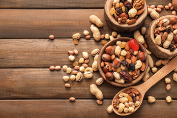 Various tasty nuts with bowls and spoon on wooden table