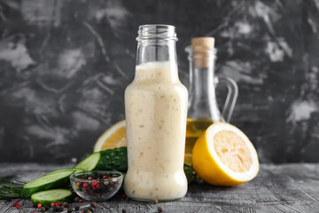 Bottle with tasty white sauce, cucumber and lemon slices on grey table