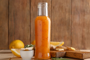 Bottle with tasty sauce, ginger and lemons on wooden table