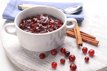 Bowl with tasty cranberry sauce and cinnamon sticks on wooden board