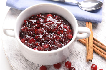Bowl with tasty cranberry sauce and cinnamon sticks on wooden board