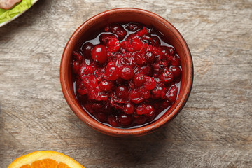 Bowl with tasty cranberry sauce on wooden background, top  view