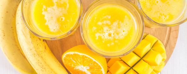 Yellow smoothie of mango, banana and orange on a white wooden table.