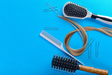 Flat lay composition with hairdresser's tools and strand of blonde hair on color background