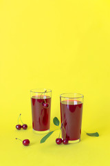 Cherry juice with cherry berries on yellow background.