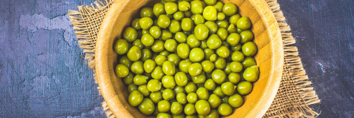 Canned peas in a wooden plate on a gray concrete background.