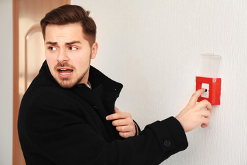 Young man pushing button of fire alarm system, indoors
