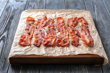 Board with tasty fried bacon on wooden table