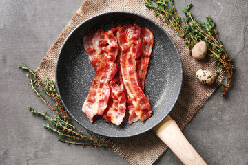 Frying pan with tasty bacon on grey background