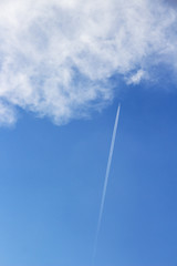 Skyscape with a plane with contrail approaching a fluffy cloud