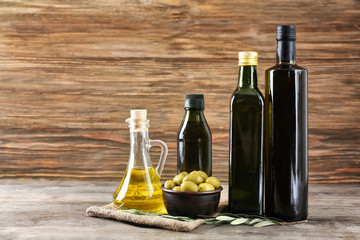 Composition with olive oil in bottles and jug on wooden background