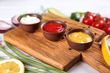Bowls with different sauces on wooden board, closeup