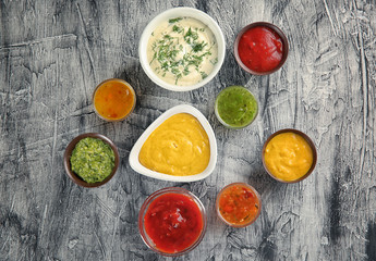 Bowls with different sauces on grey textured background, top view