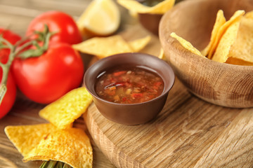 Bowl with tasty sauce and nachos on wooden board, closeup