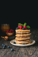 Stack of pancakes topped with fresh berries and honey on rustic wooden table. Homemade pancakes with raspberries and blueberries. Copy space for text