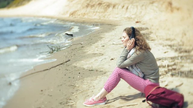 A woman listens to music on headphones, relaxes and dances on the shore of the sea river of the ocean. Technology in the open air