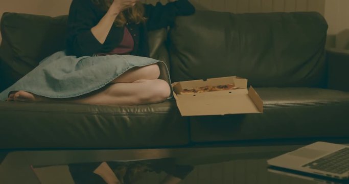 Woman at home eating pizza and watching film on laptop