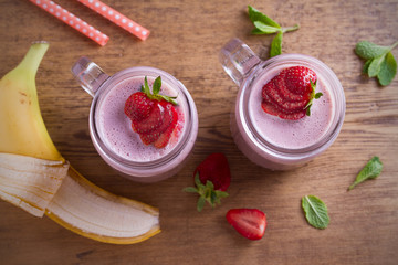 Two glasses of pink strawberry milkshake or cocktail. Strawberry banana smoothie on wooden table. overhead, horizontal